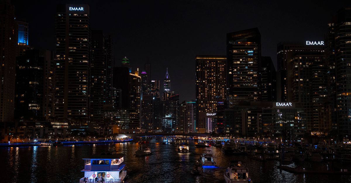 Illuminated Dubai Marina skyline at night with boats on the water.