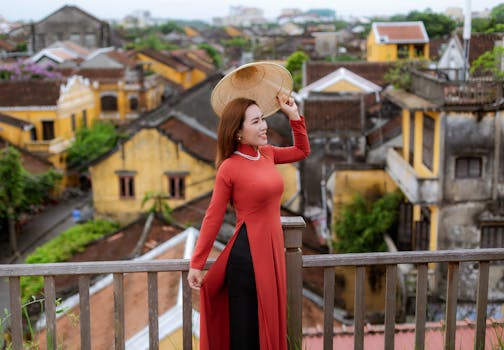 Woman wearing an áo dài and nón lá overlooks Hội An's charming ancient town rooftops.