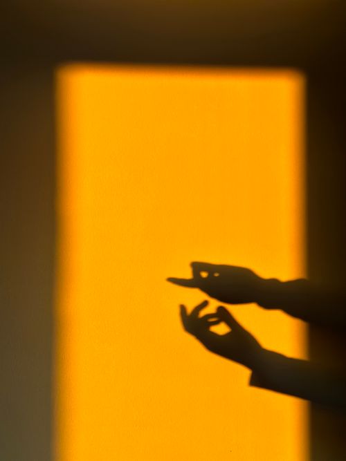 Free Abstract shadows of hands gesture dynamically against a vibrant yellow background. Stock Photo