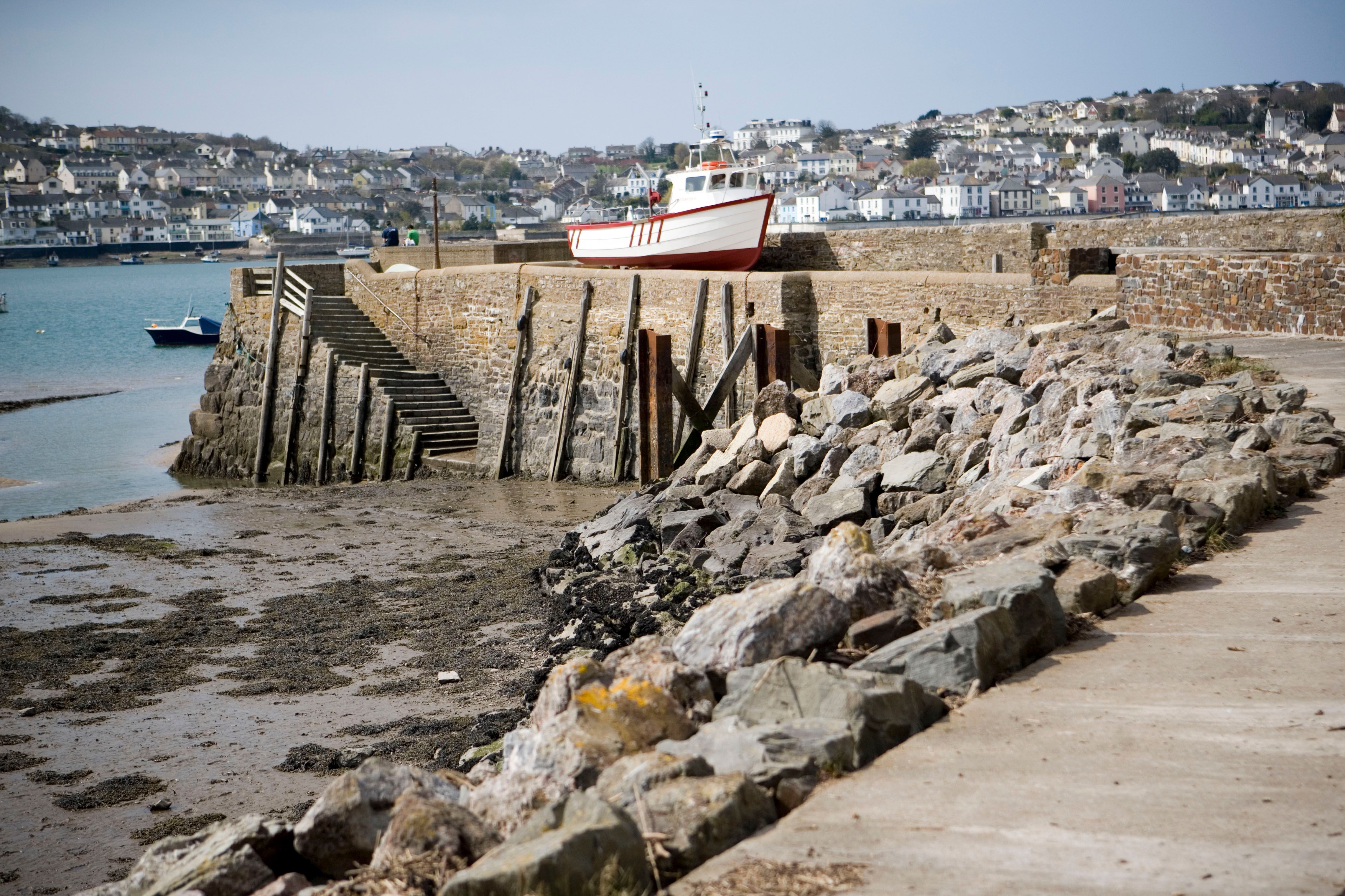 A peaceful harbor scene in England with a boat docked at the stone pier and a distant town view.