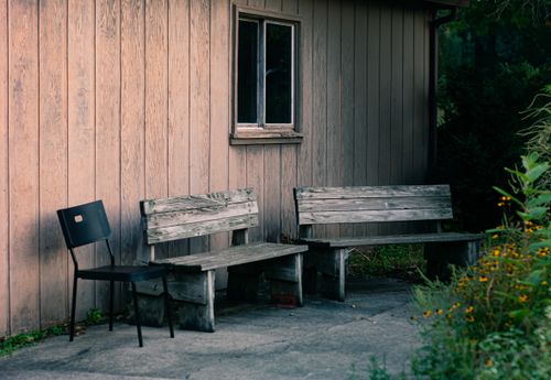 Free Charming outdoor scene with rustic wooden benches and a modern chair against a wooden wall. Stock Photo