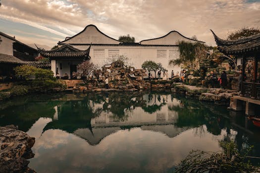 Tranquil scene of a Suzhou garden with a reflective pond under a cloudy sky.