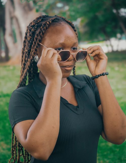 Free Casual portrait of a young woman in the park adjusting sunglasses on a sunny day. Stock Photo