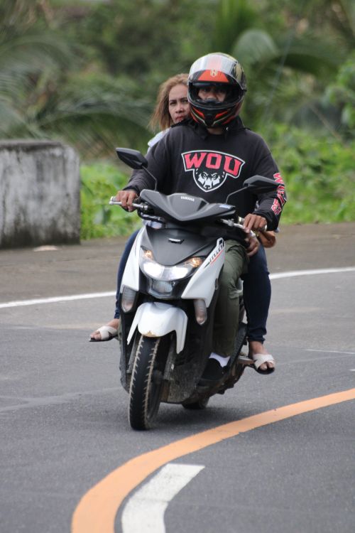 Free Two people riding a motorbike on a curved road, showcasing outdoor travel. Stock Photo