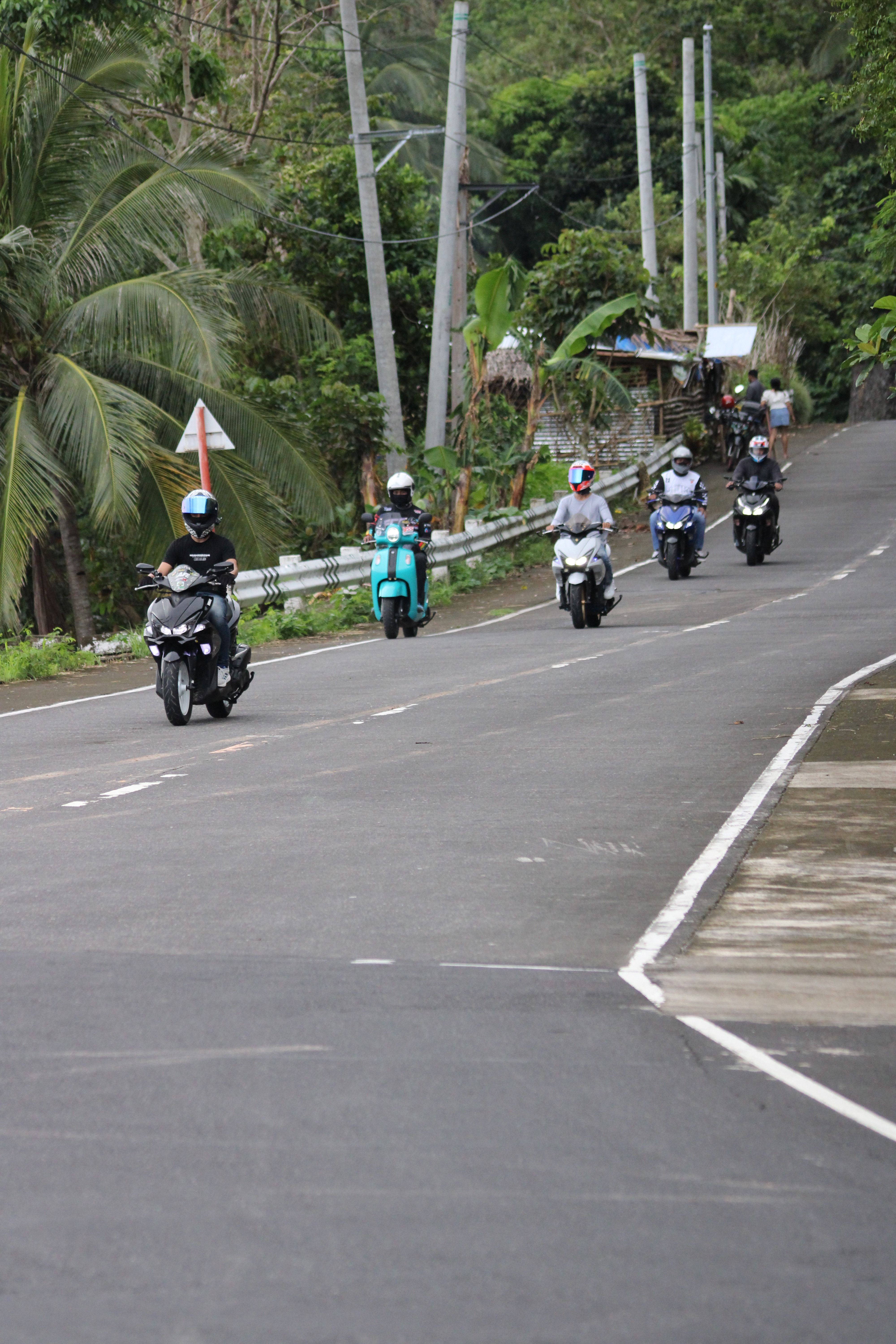 Five motorcyclists riding down a lush, tropical road, showcasing outdoor adventure.