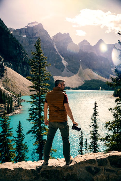 Man Standing on a Stonewall looking at the Mountains and Body of Water