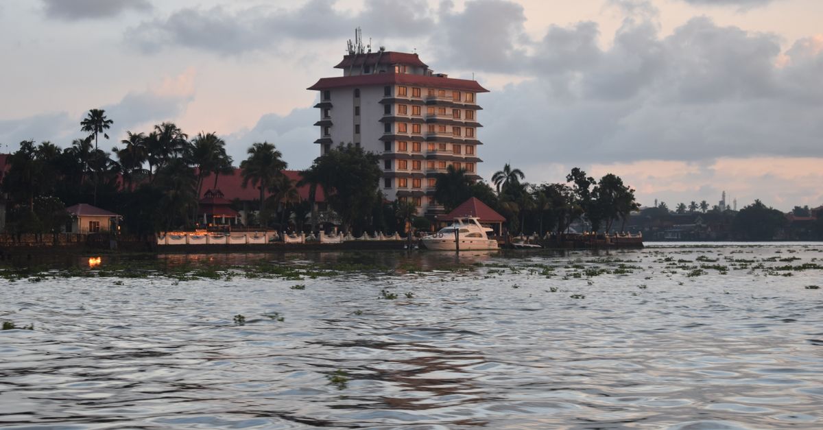 Serene riverside scene featuring a multi-story hotel and palm trees at sunset.