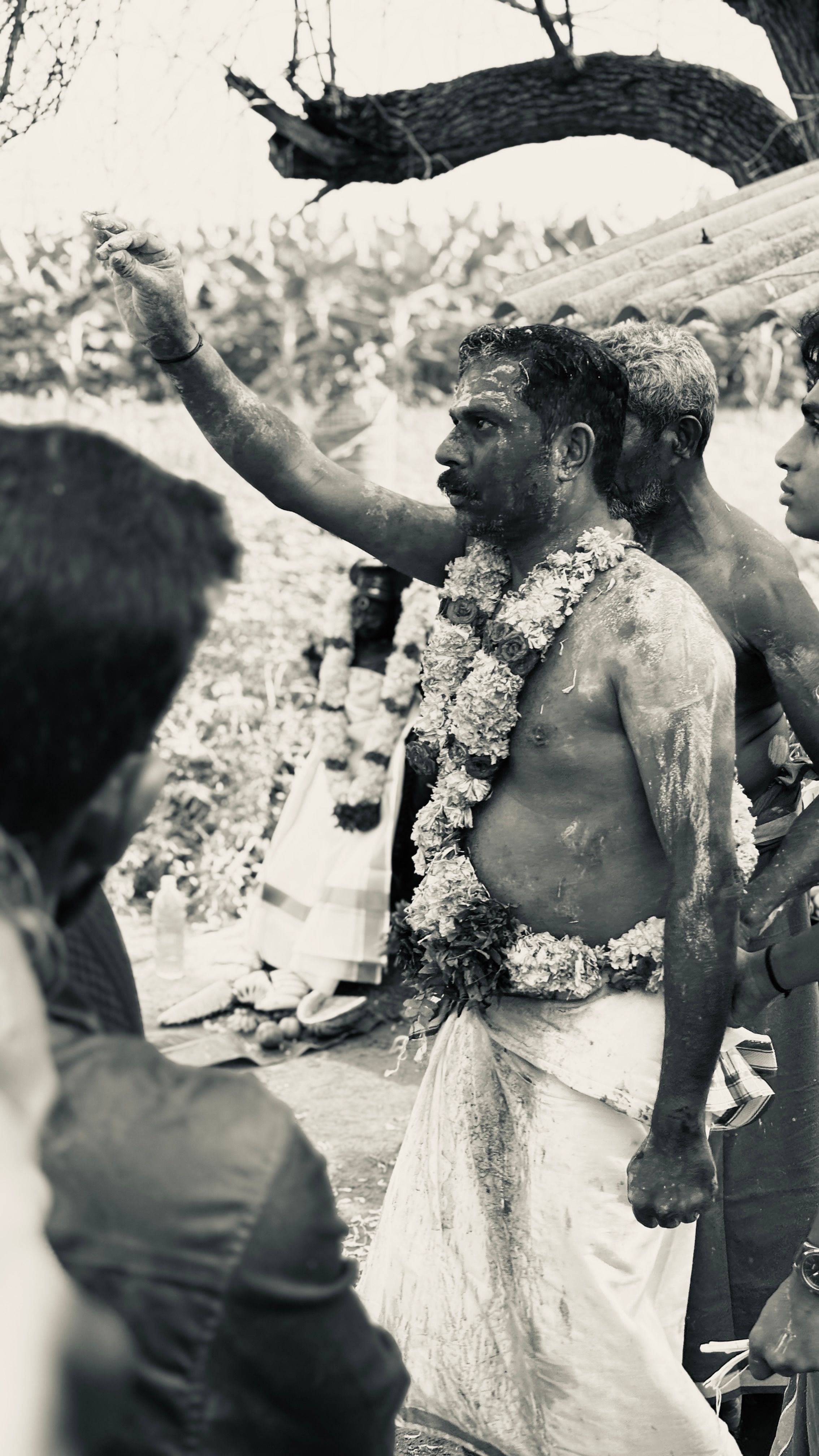 A monochrome image of a man adorned with garlands participating in a traditional ritual outdoors.