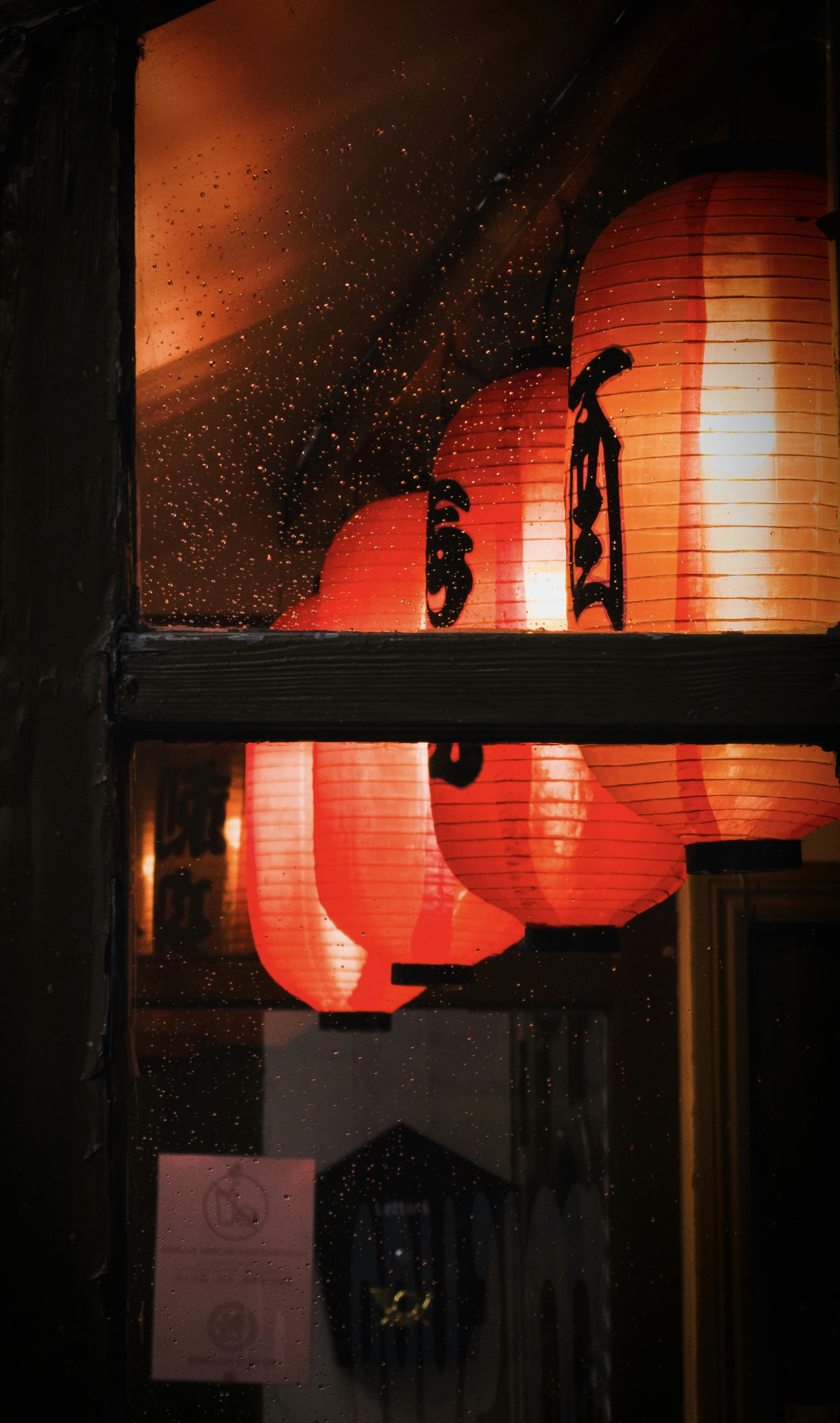 grátis Brilho quente das tradicionais lanternas de papel japonesas através de uma janela chuvosa à noite. Foto profissional