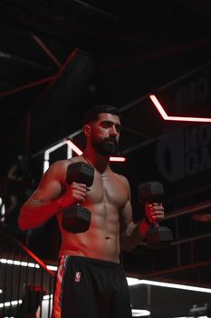 Muscular man exercising with dumbbells in a modern gym setting under dramatic lighting.