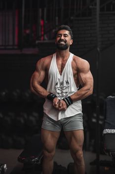 A muscular man confidently poses in a gym setting, showcasing his strength and physique.