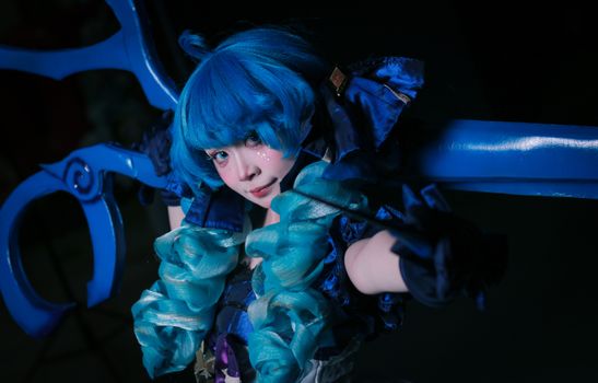 Anime-inspired cosplay with bright blue hair, costume, and oversized scissors prop.