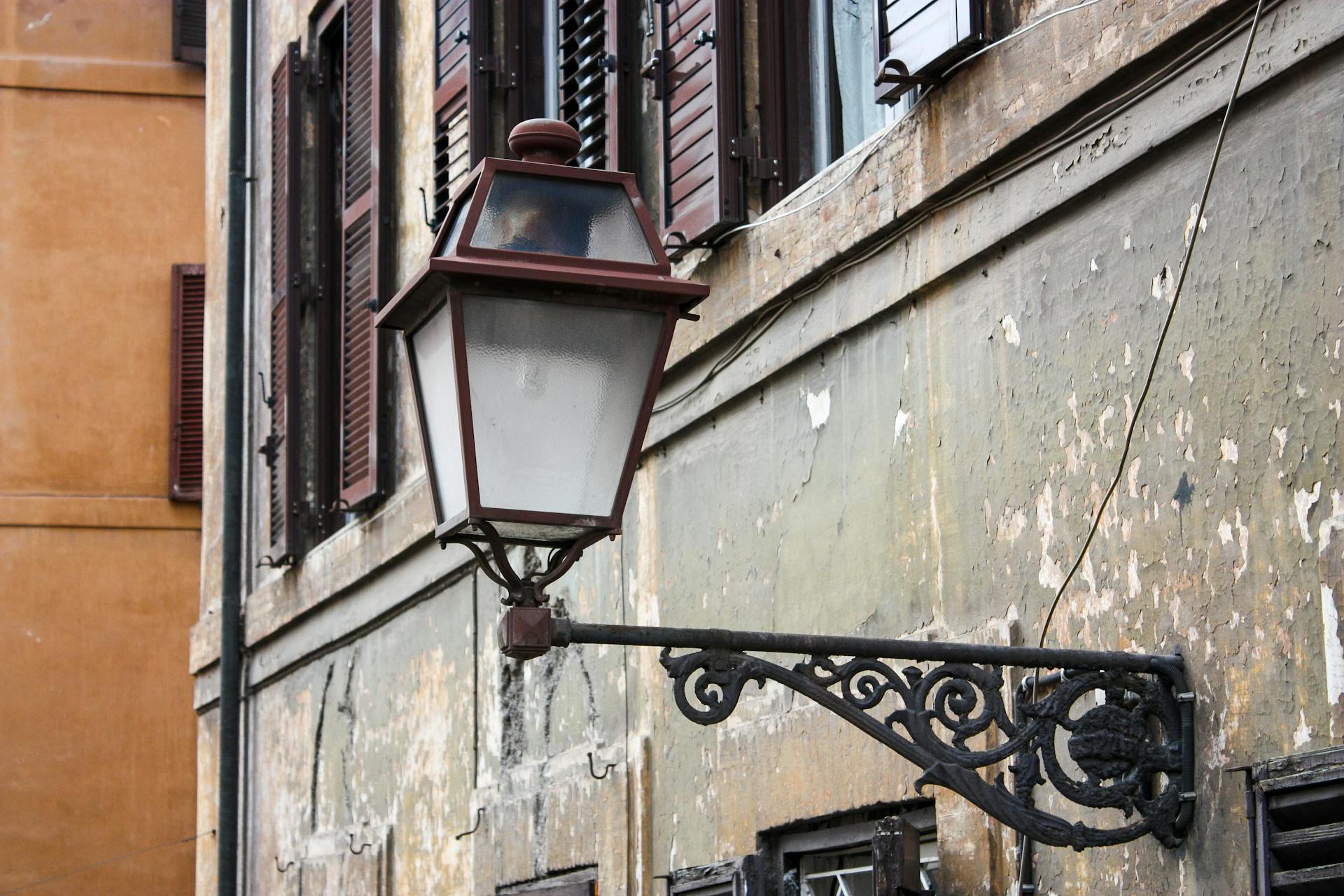 Rustic street lamp on an aged facade in Rome, capturing the charm of historic architecture.