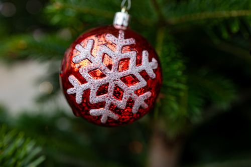 Free Close-up of a red Christmas ornament with a snowflake pattern hanging on a tree. Stock Photo