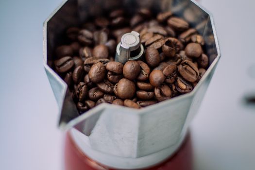 High-angle view of roasted coffee beans in a stainless steel Moka pot, ready for brewing.