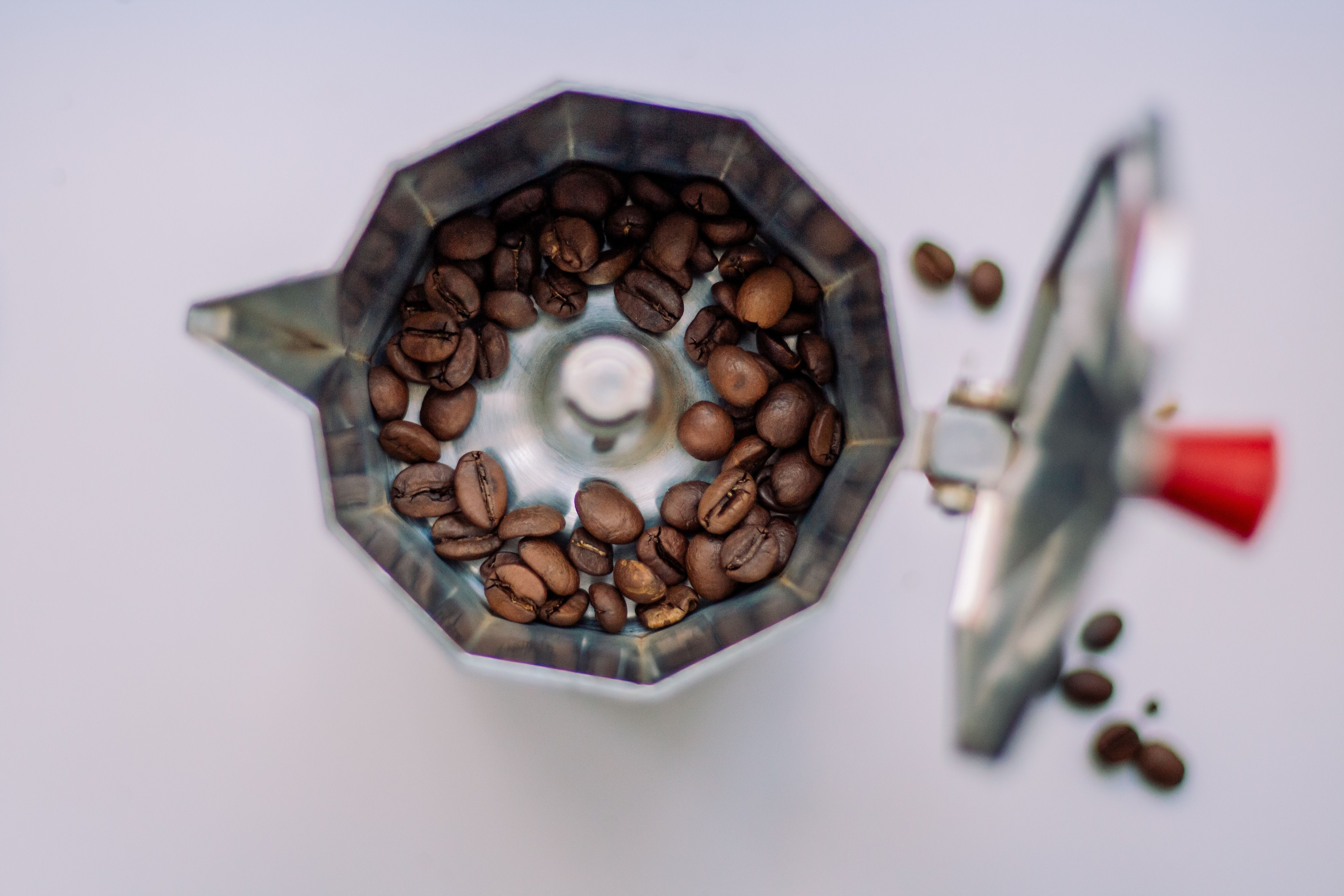 Aerial shot of coffee beans in a moka pot on a white background.