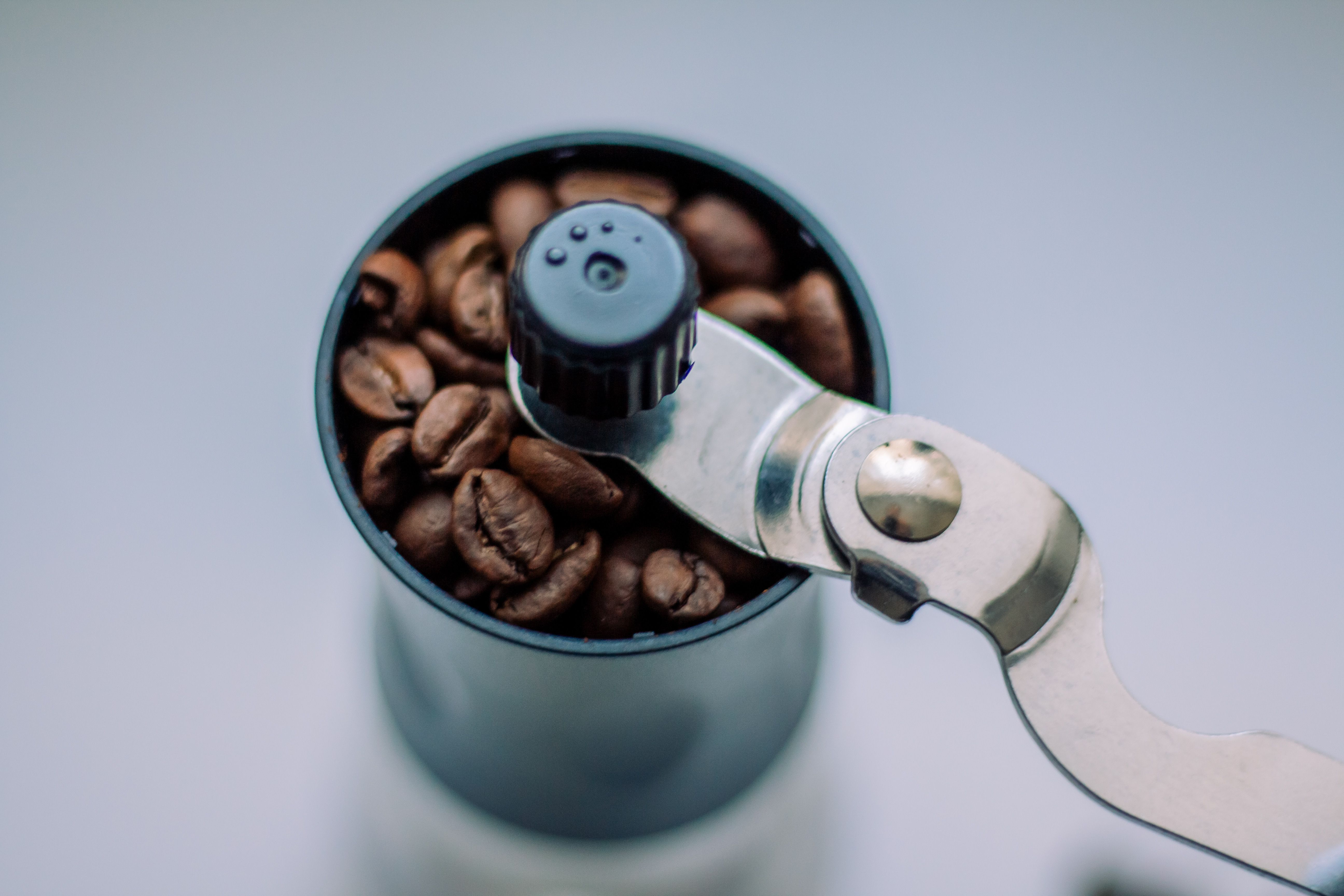 Manual coffee grinder filled with fresh roasted coffee beans, top view.