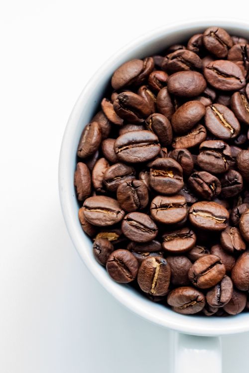 Free A white cup filled with roasted coffee beans on a light background. Stock Photo