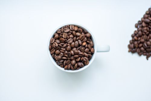 Free Overhead view of a cup filled with roasted coffee beans on a white surface. Stock Photo