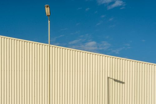 Free Minimalist photo of a modern industrial building facade with streetlamp shadow under a blue sky. Stock Photo