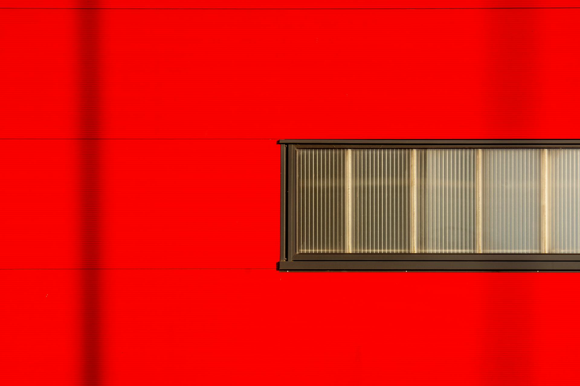 A striking minimalist photograph of a red wall featuring a horizontal window. Perfect for modern design inspiration.