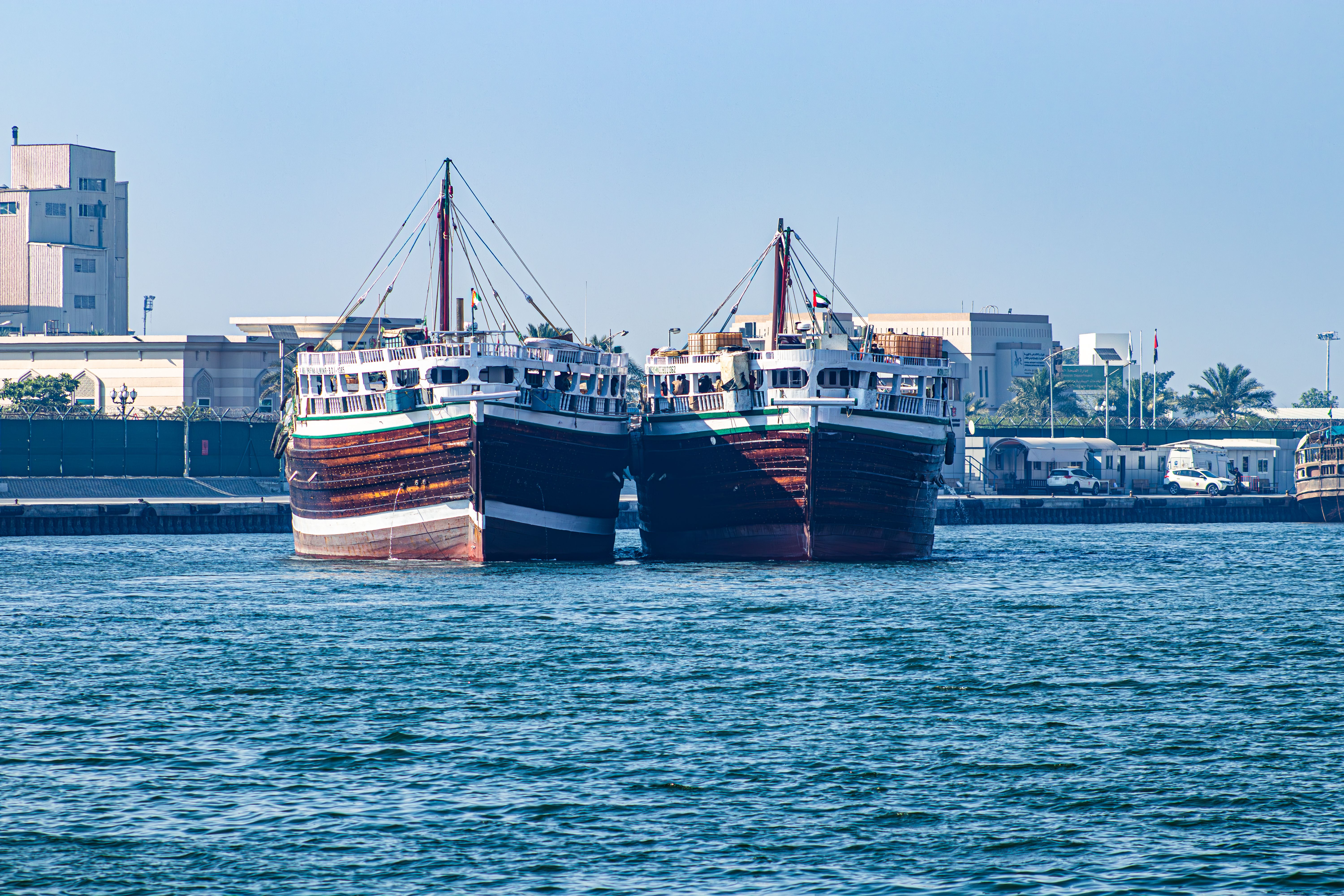Two traditional boats docked at a harbor in Sharjah, UAE, under a clear blue sky.