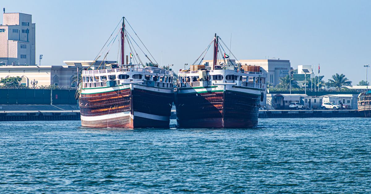 Two traditional boats docked at a harbor in Sharjah, UAE, under a clear blue sky.