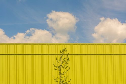 Free Bright yellow wall against a blue sky with clouds, showcasing modern architecture. Stock Photo