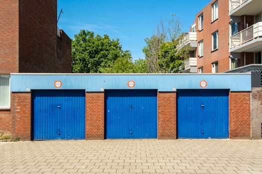 Three blue garage doors in a brick building on a sunny day.