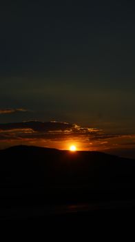 A beautiful sunset over rolling hills, silhouette against a vibrant sky.