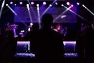 在充满活力的现场音乐会期间，一名音响工程师管理着灯光丰富多彩的音频混音器