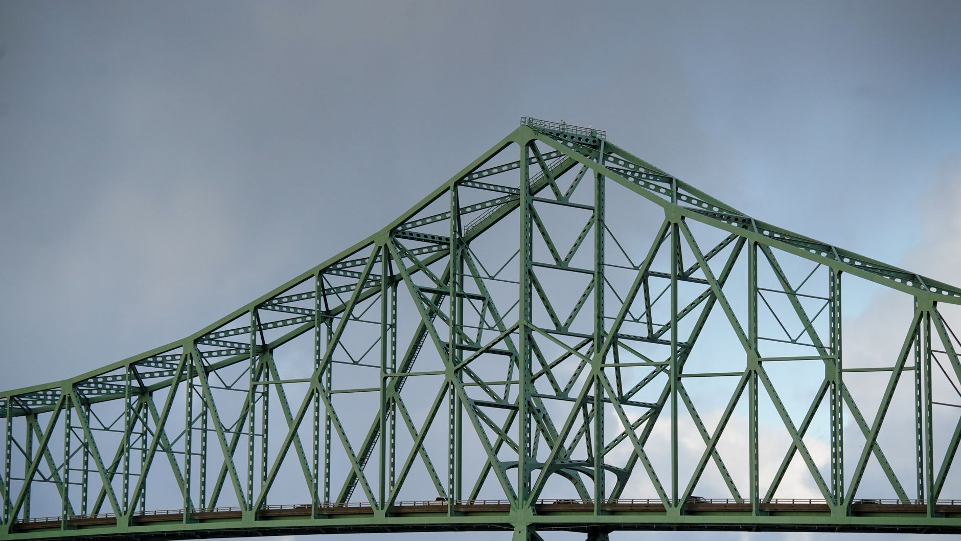 Close-up view of a green steel truss bridge against a cloudy sky, showcasing architectural design. — free online jigsaw puzzle on JigsawPuzzlesFreeOnline.org