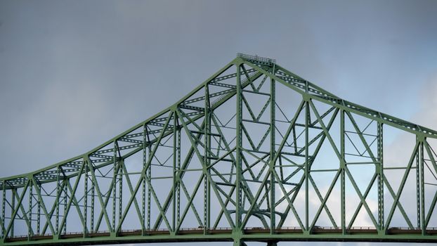 Close-up view of a green steel truss bridge against a cloudy sky, showcasing architectural design., free online jigsaw puzzle on JigsawPuzzlesFreeOnline.org
