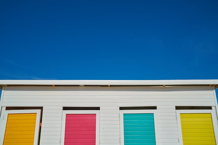 White Wooden House With Yellow, Pink, Green, And Orange Painted Windows