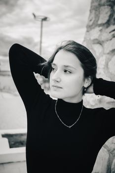 Black and white portrait of a young woman in a thoughtful pose outdoors.