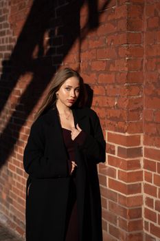 A fashionable woman poses confidently against a sunlit brick wall, exuding elegance.