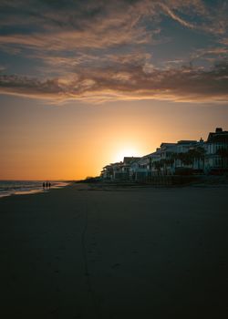 Peaceful sunset view over beachfront homes with calm sea and colorful sky.