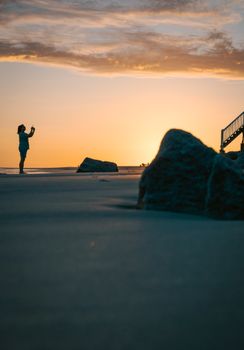 Silhouette of a woman on a beach capturing the sunset. Peaceful and serene ambiance.