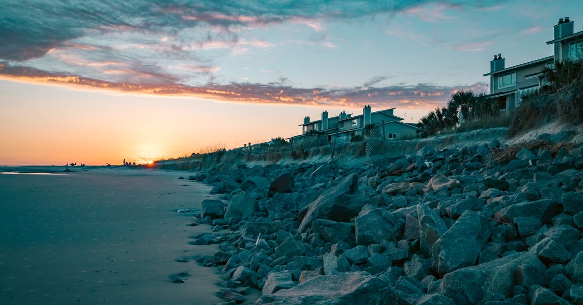 Beautiful sunset view over beach with rocky shore and coastal homes under a vibrant sky.