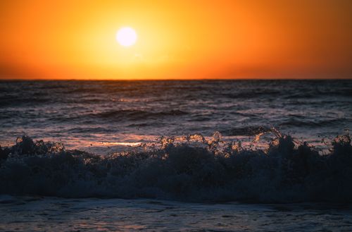 Free Beautiful ocean sunset with vibrant orange sky and waves crashing on shore. Stock Photo