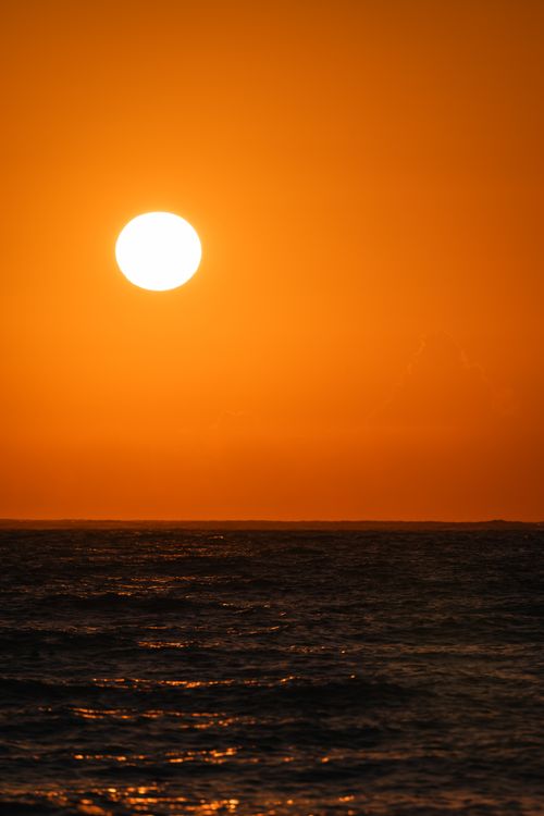 Free A mesmerizing ocean sunset with a vivid orange sky and the sun setting over the horizon. Stock Photo