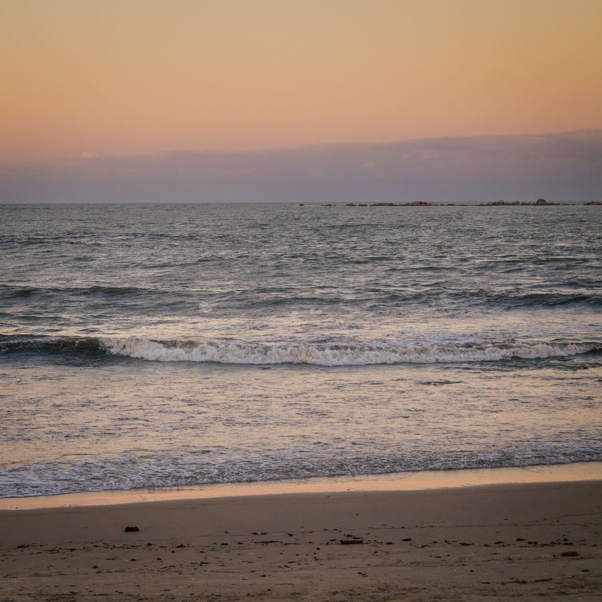 Sunset over calm surf and open sand — photo by JUNIOR FOSSILE on Pexels