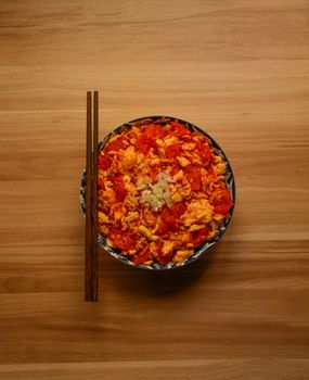 Bowl of delicious tomato and egg stir fry with chopsticks on wooden table.