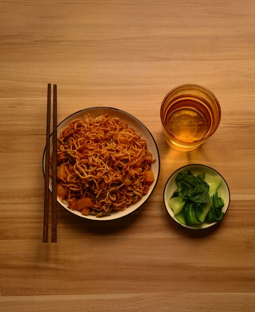 Free Top view of a noodle bowl with chopsticks, salad, and tea on a wooden table. Stock Photo