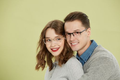 Free Charming couple wearing fashionable glasses, embracing against a soft green backdrop. Stock Photo