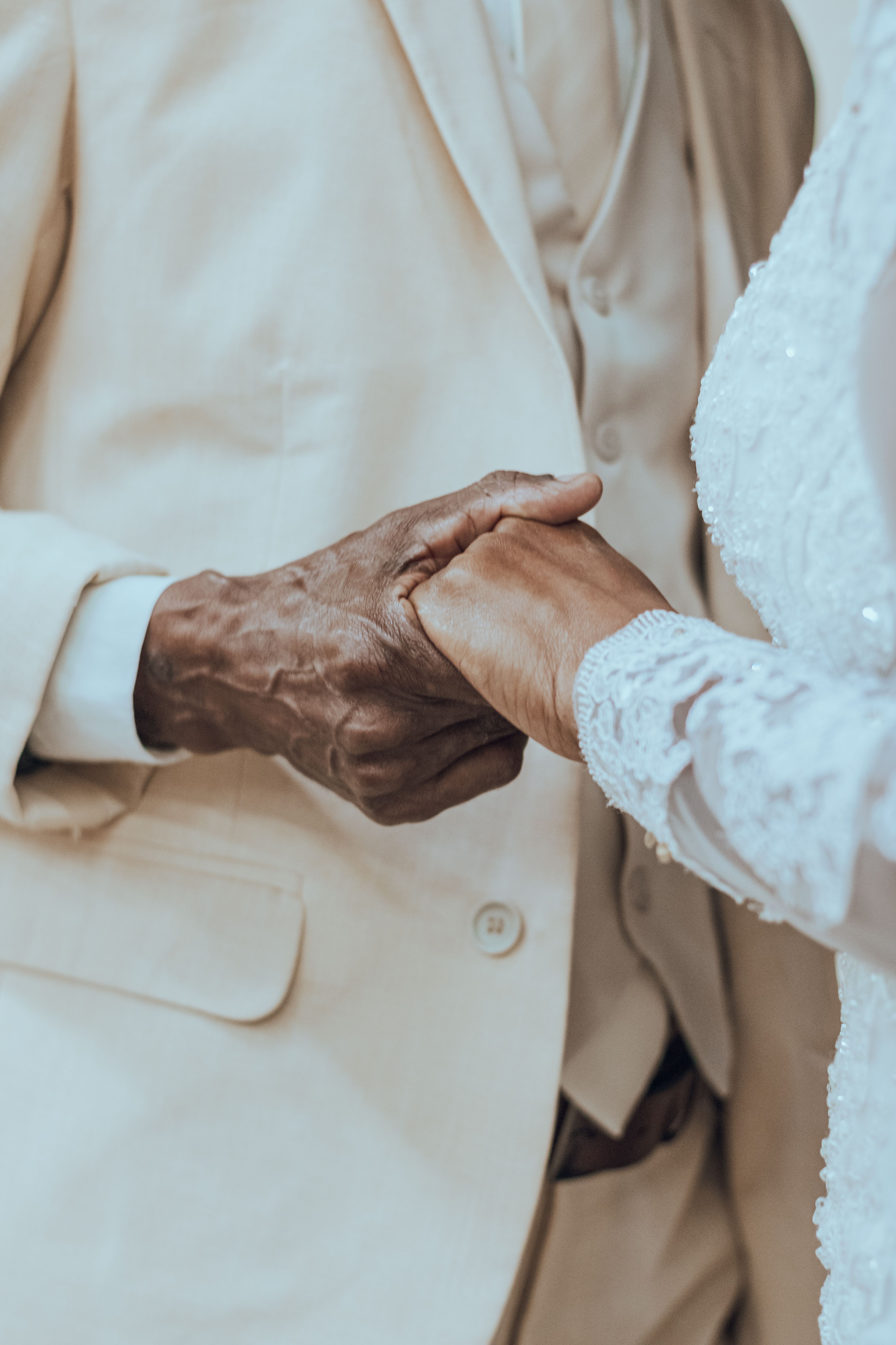 An intimate moment captured between an elderly couple holding hands during a wedding ceremony close-up.
