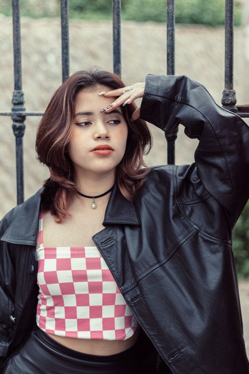 Free Young woman poses in a leather jacket and checkered top against an iron fence outdoors. Stock Photo