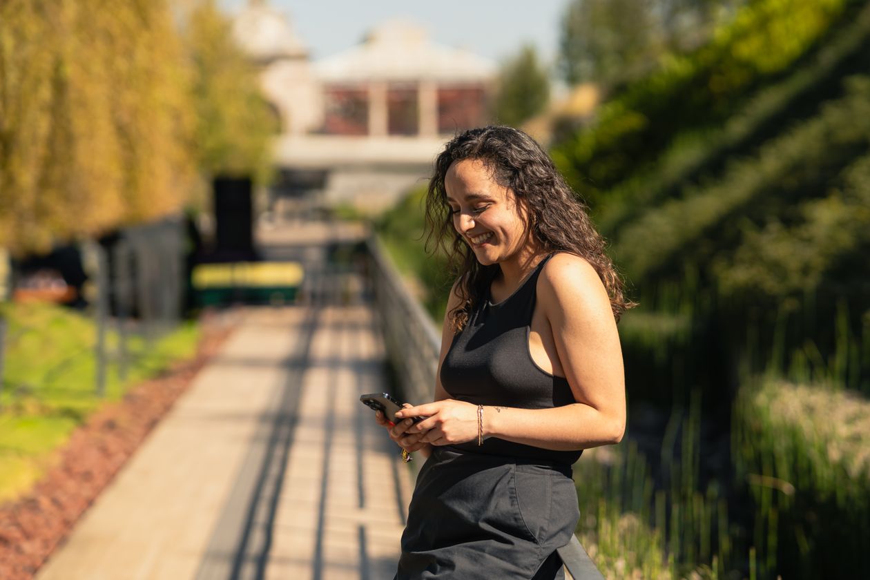 A young woman smiling while texting on her phone in a park