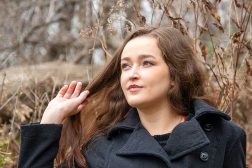 Free Woman with long hair poses in nature wearing a black coat, showcasing beauty. Stock Photo