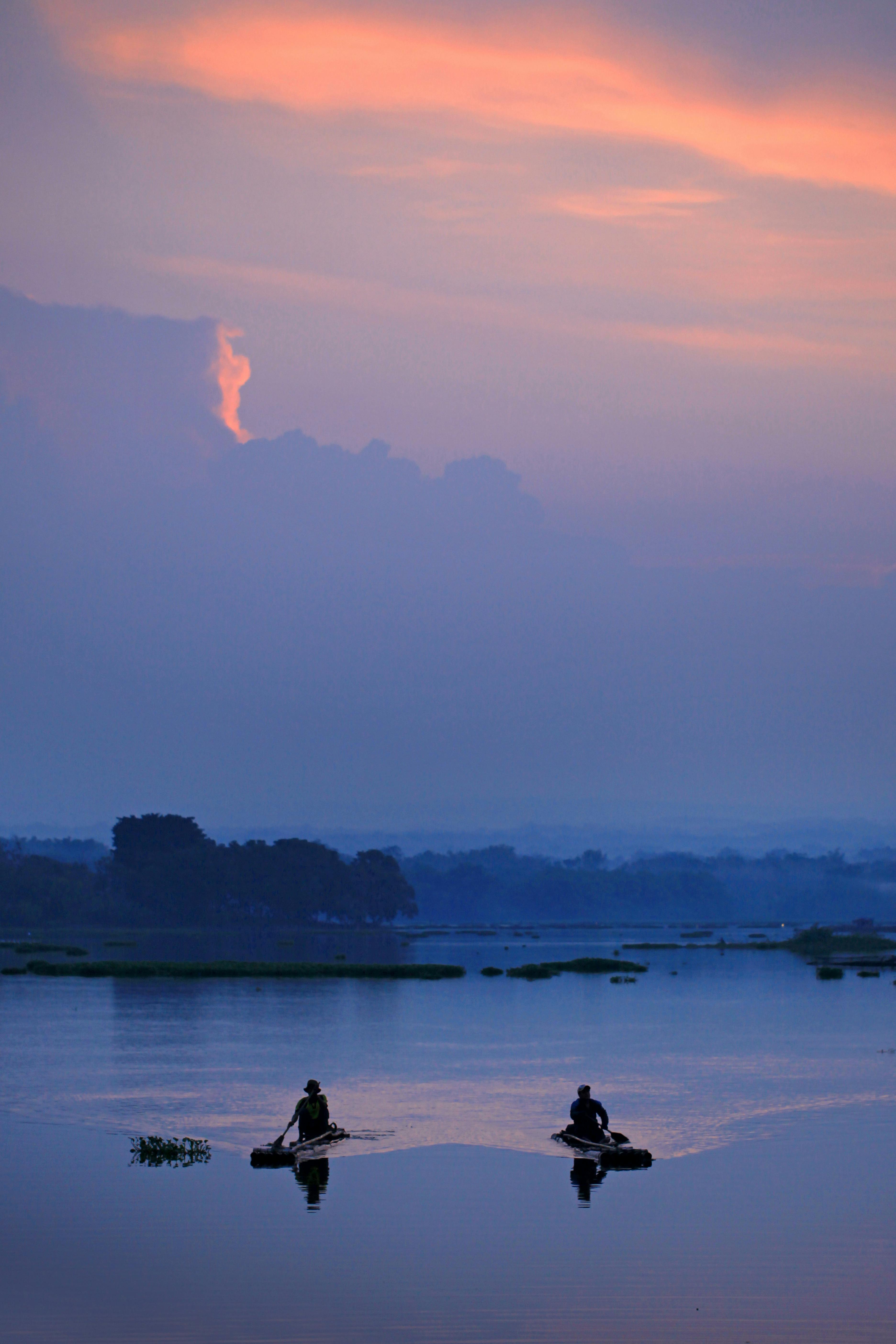 Fishermen on tranquil lake at sunrise with vibrant sky, reflecting serene morning routine.